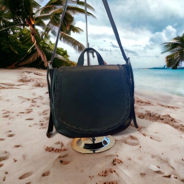 Black leather crossbody bag on beach.