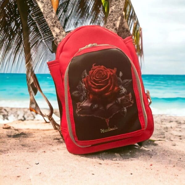 Red backpack with rose design on beach.