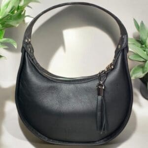 Black leather handbag with tassel detail and rounded shape.